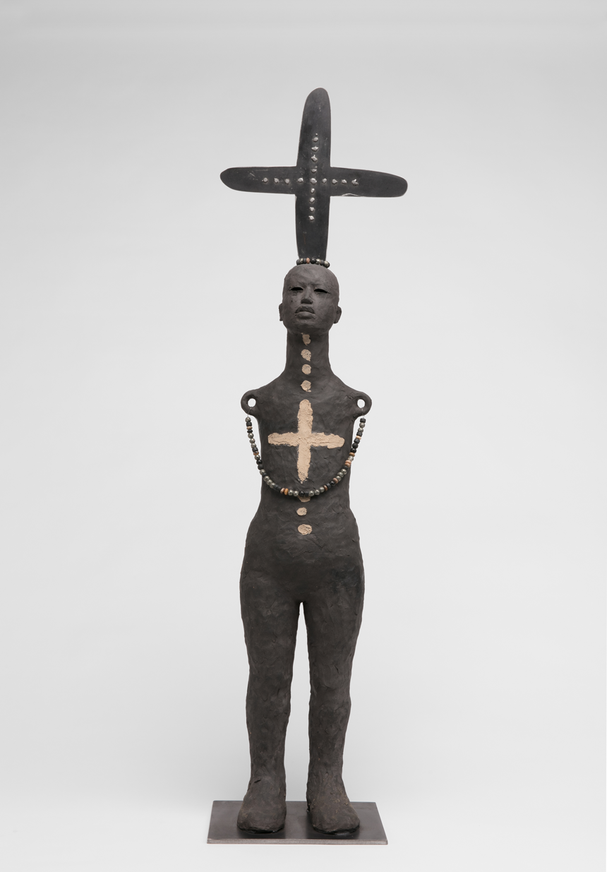 A black life-sized sculpture of a person with a cross on their head and chest