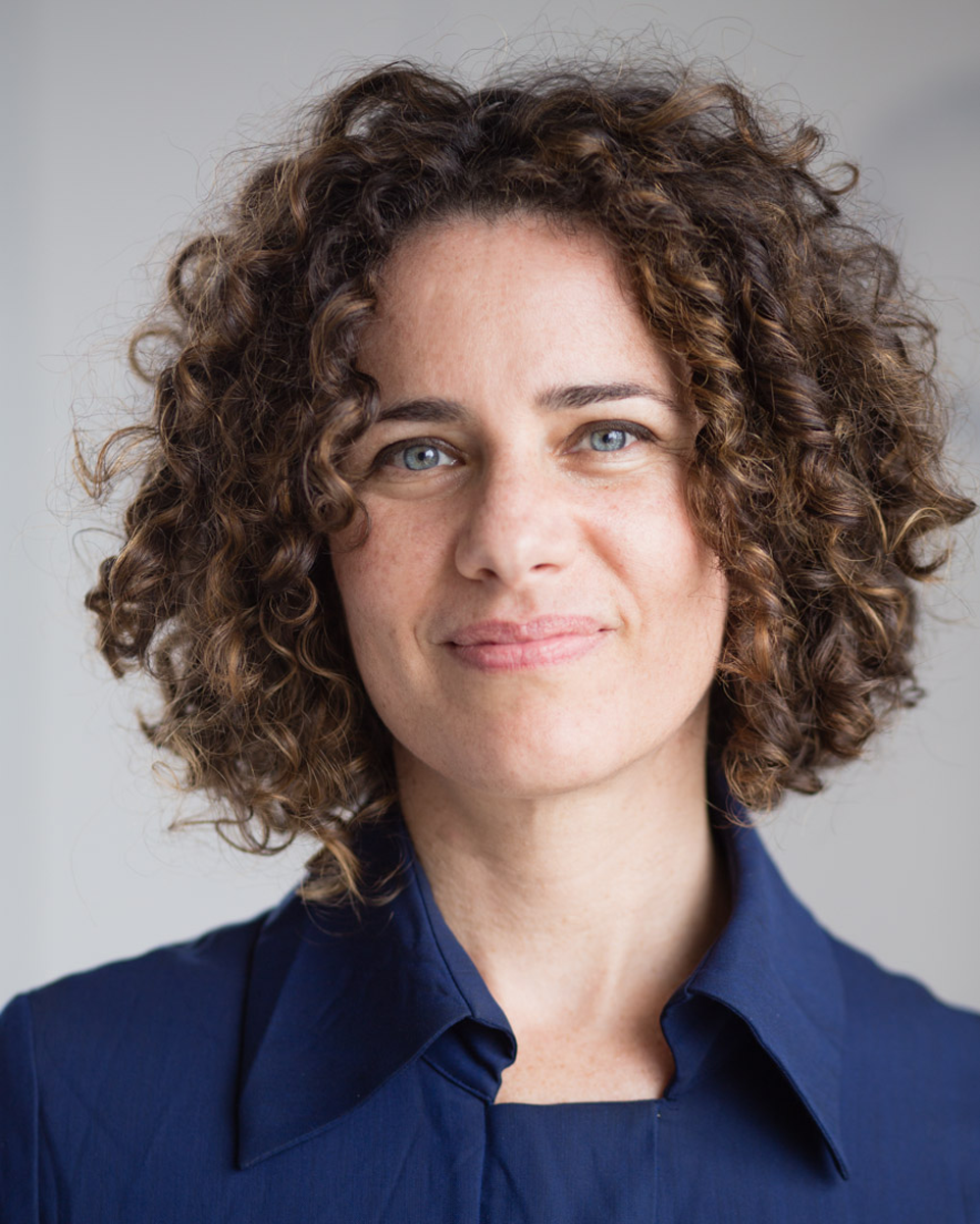 Woman with curly hair and light eyes wearing a dark blue colored shirt