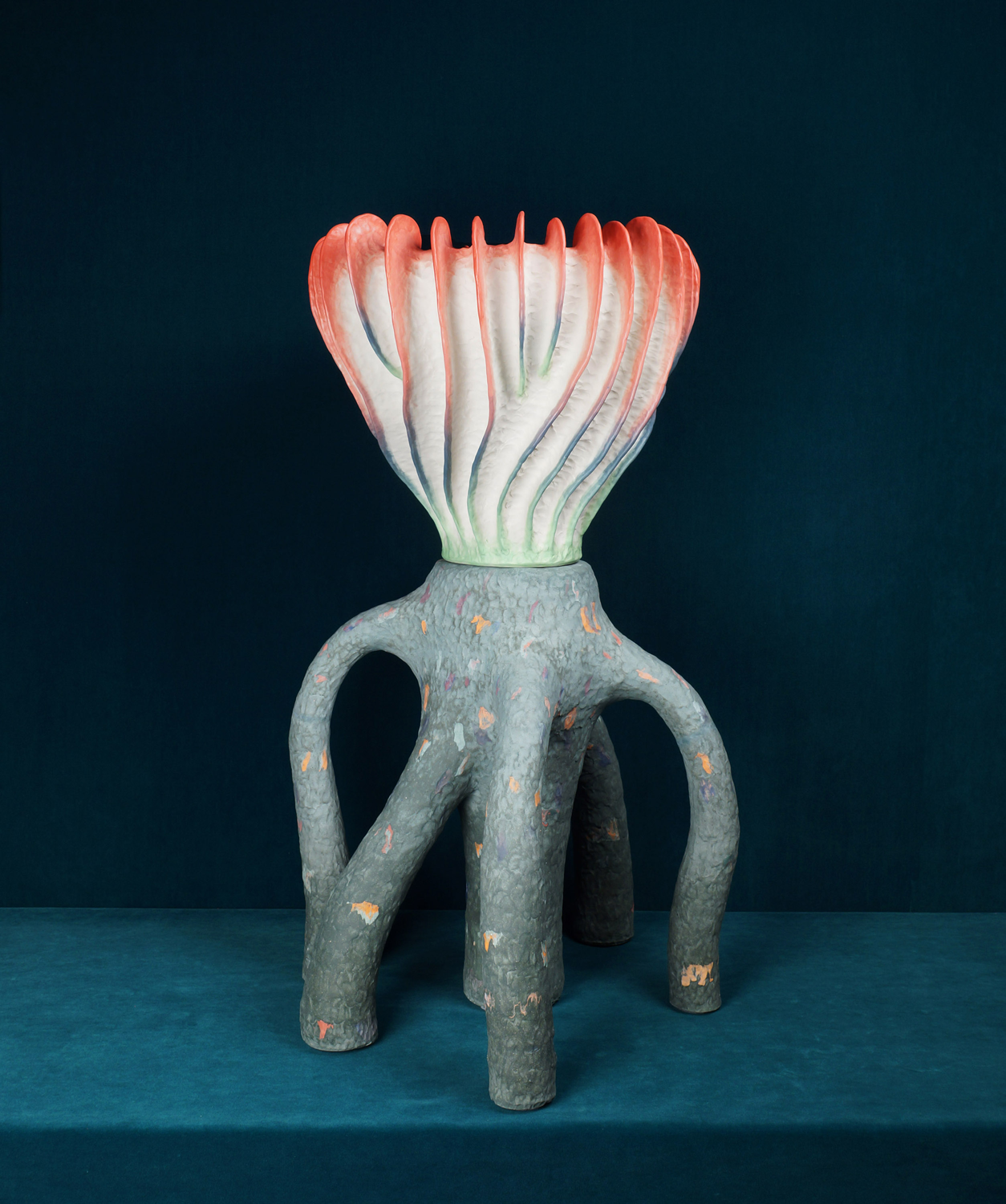 A gray six-legged ceramic vessel with white and pink protrusions at the top