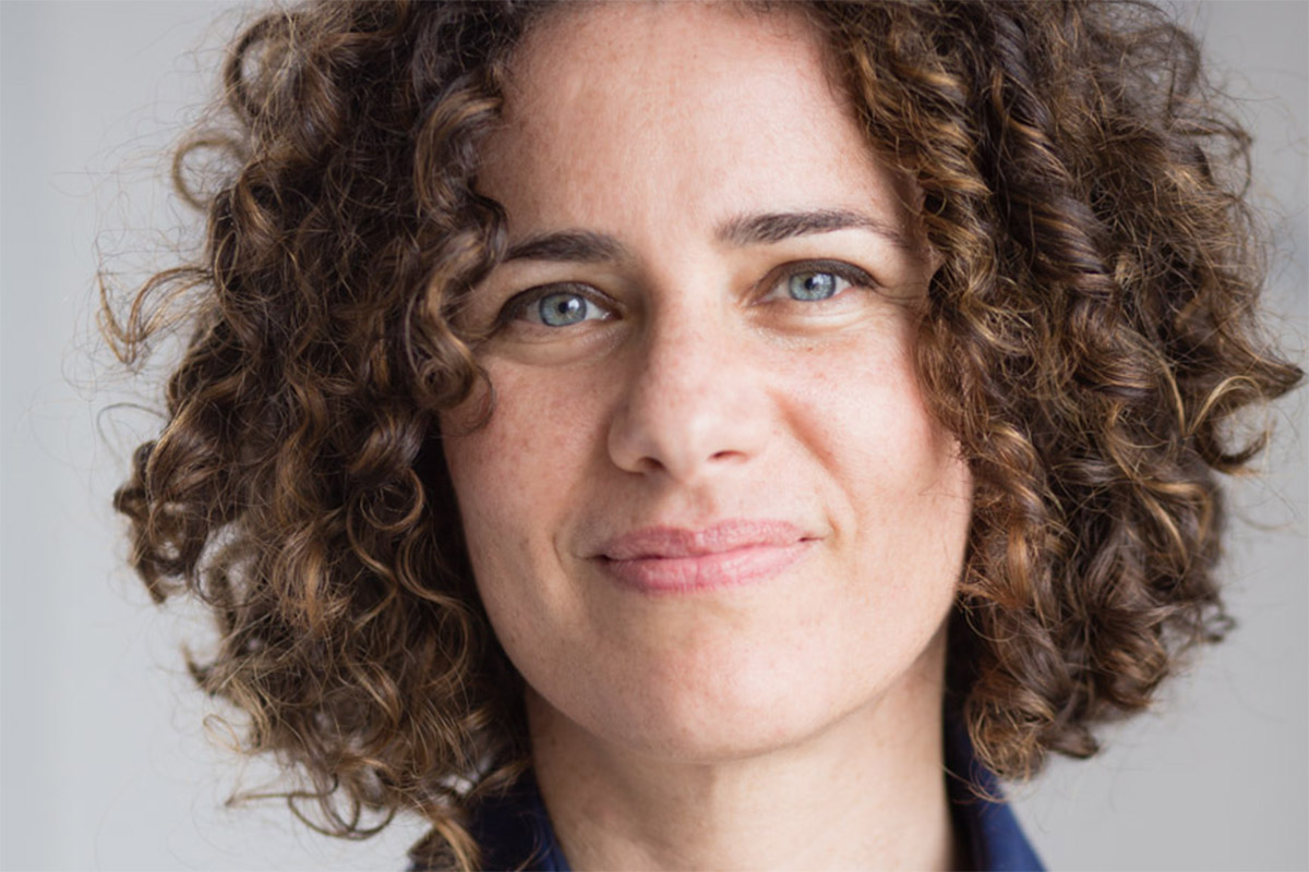 Woman with curly hair and light eyes wearing a dark blue colored shirt