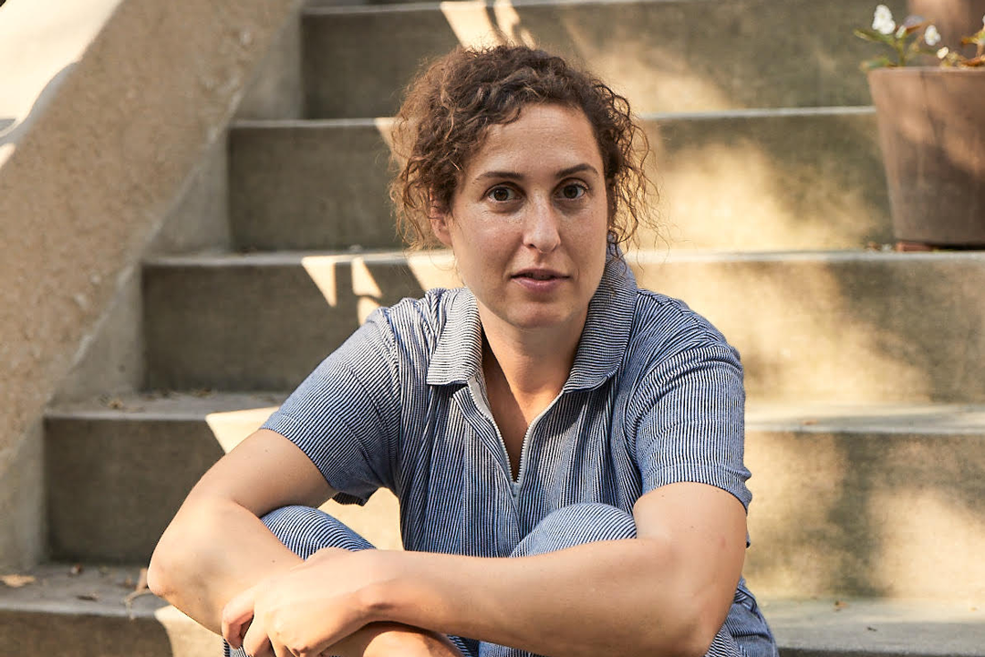 Woman in a light blue jumper with curly hair sitting on concrete steps
