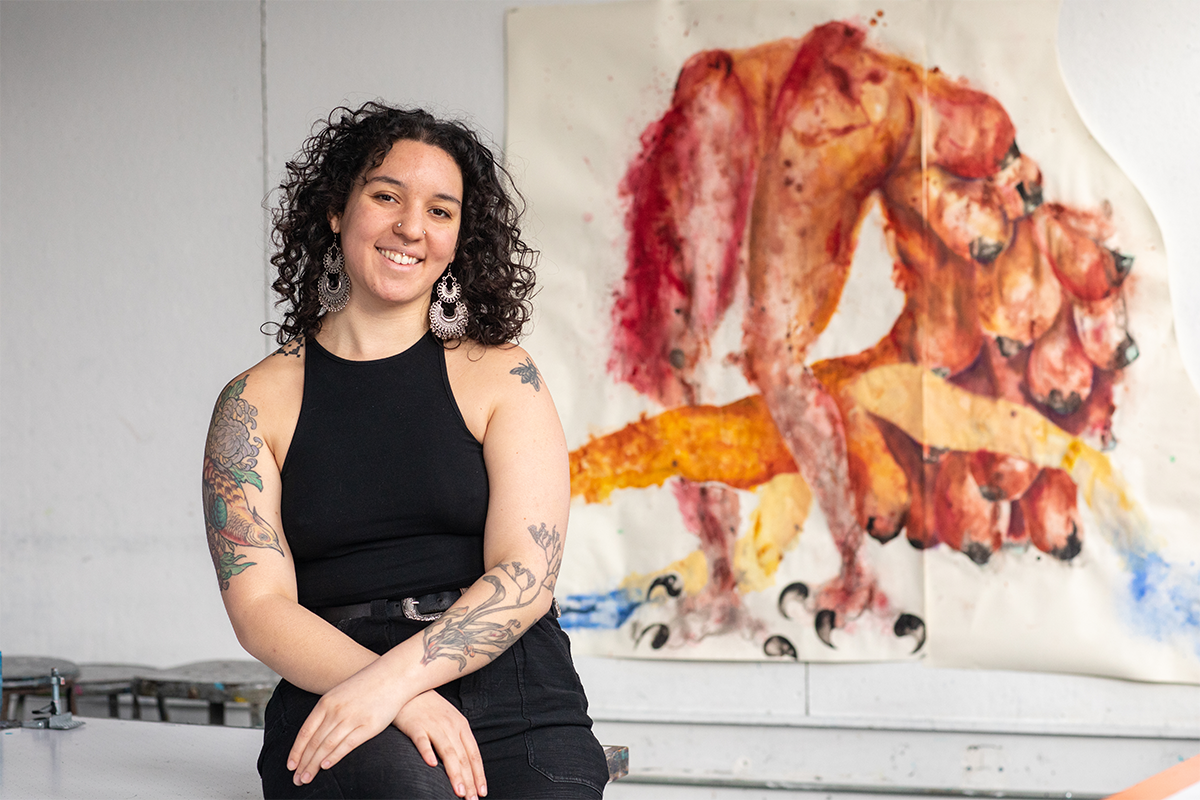Student in a sleeveless black dress with tattoos in a painting studio