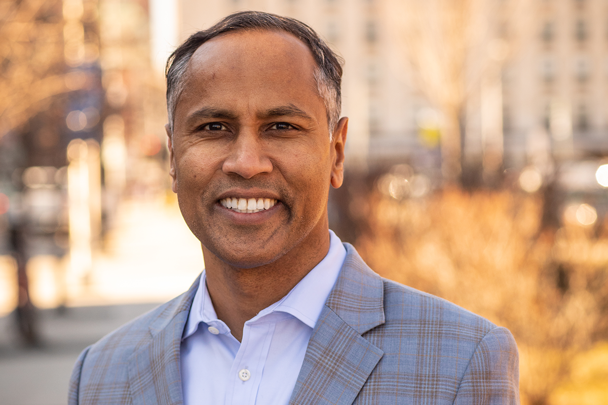 Image of a male with a grey plaid suit jacket and light blue shirt standing outdoors