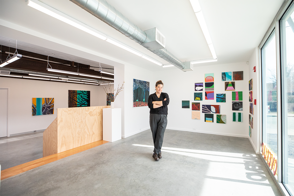 Image of a student in dark green pants and a black shirt standing in a gallery space