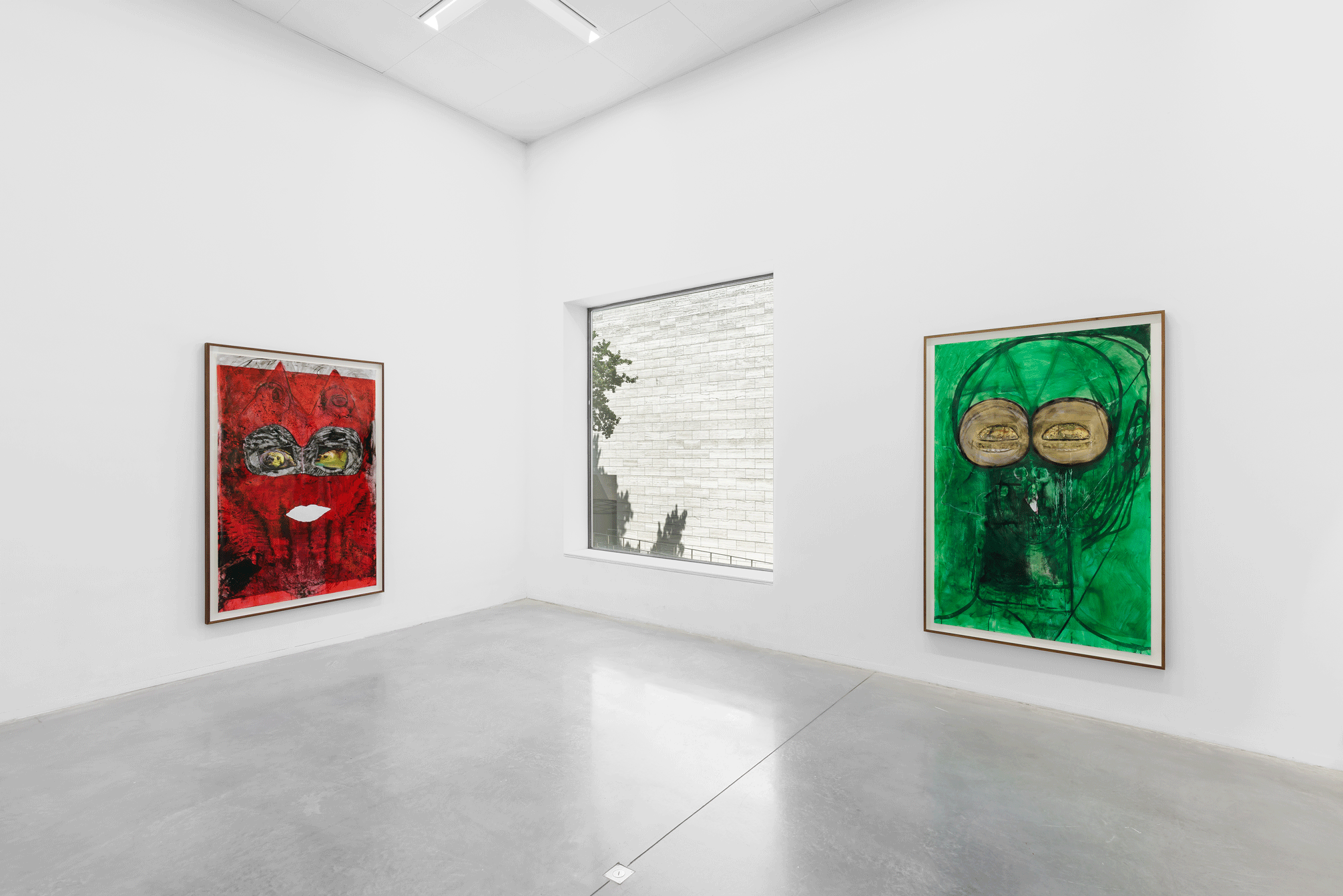 One red and one green painting of a human face in a gallery