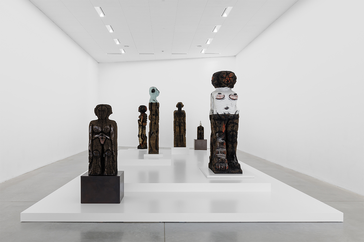 Installation view of an exhibition, with several brown figures elevated on a white platform