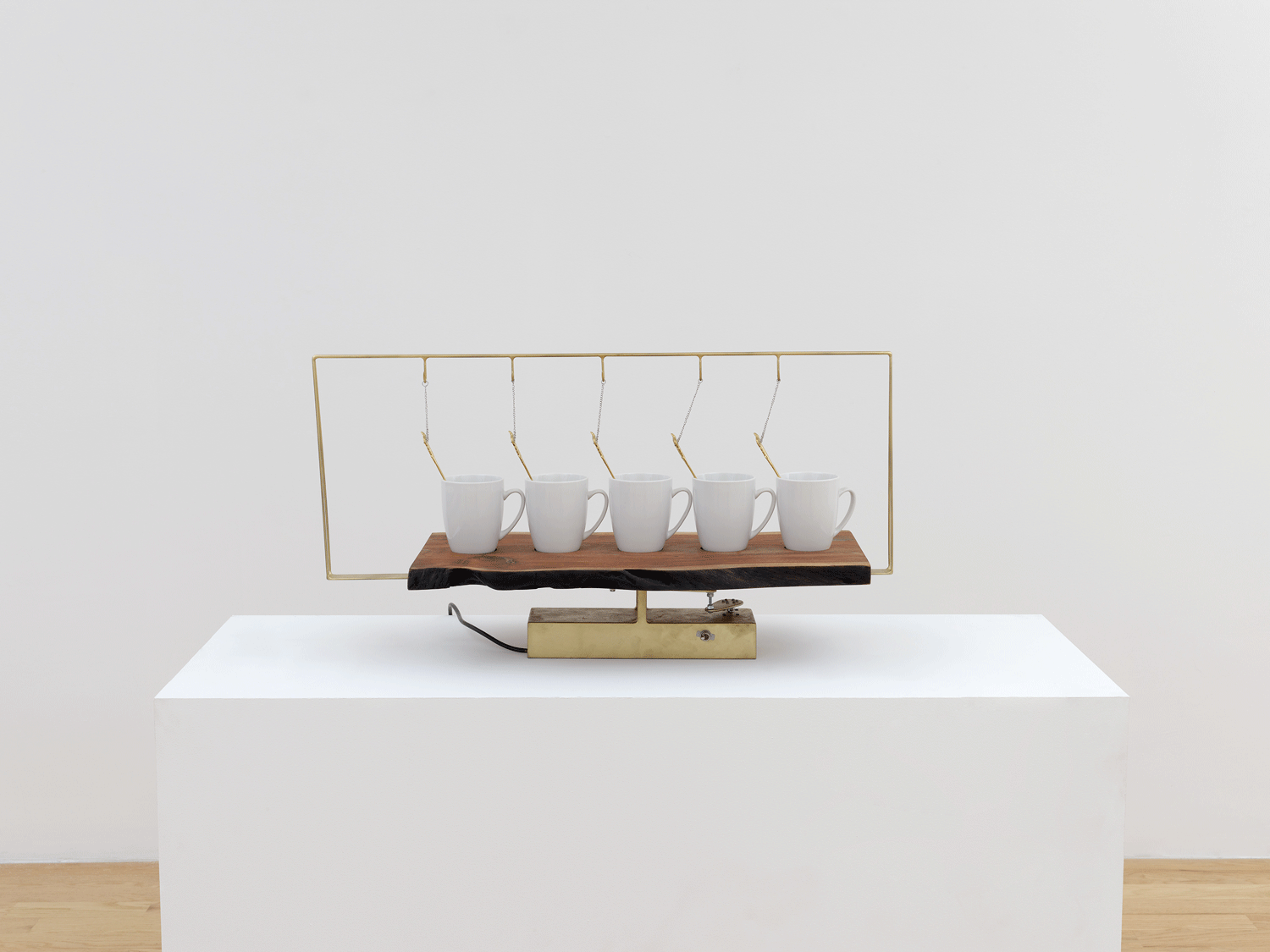 Five white coffee mugs with golden spoons, the mugs held up by golden hooks 