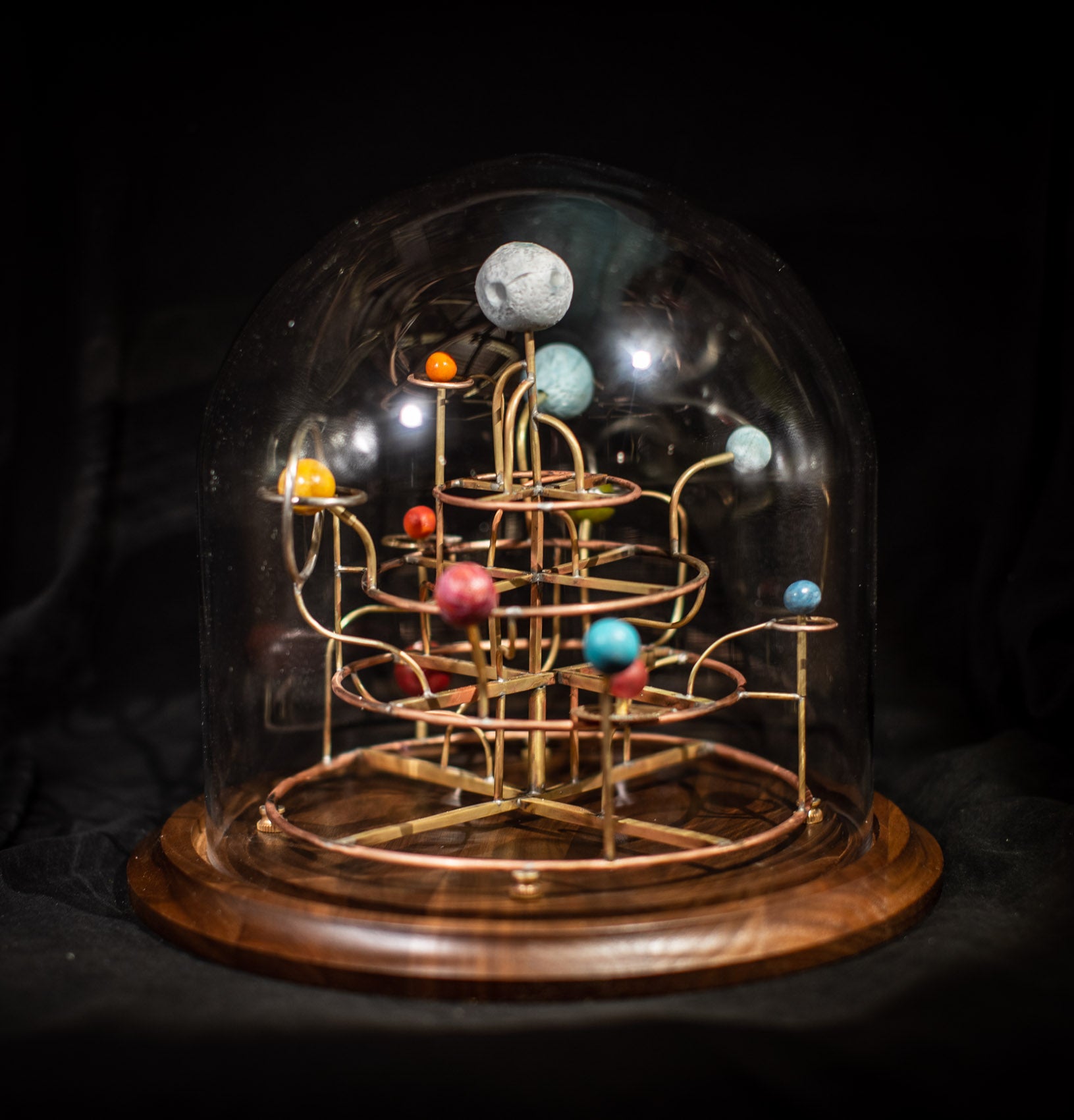 A diorama of a planetary system, with curved brass rods holding up planets crafted from clay