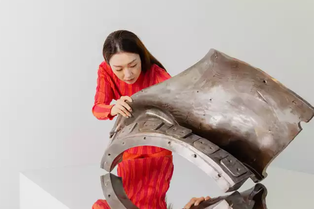 Xin Liu in red working on a metal sculpture in a white room