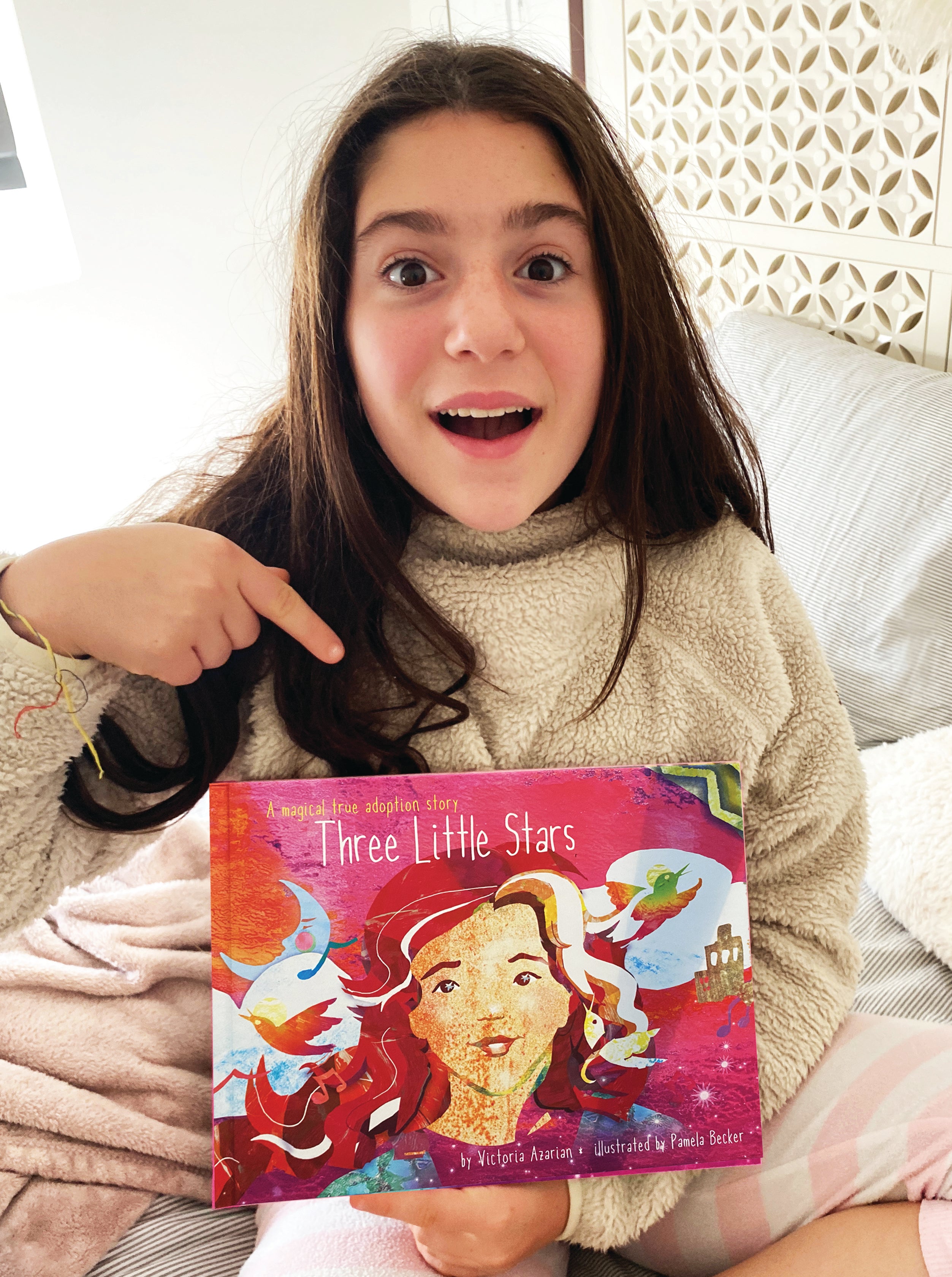 An image of a young girl holding a copy of "Three Little Stars"