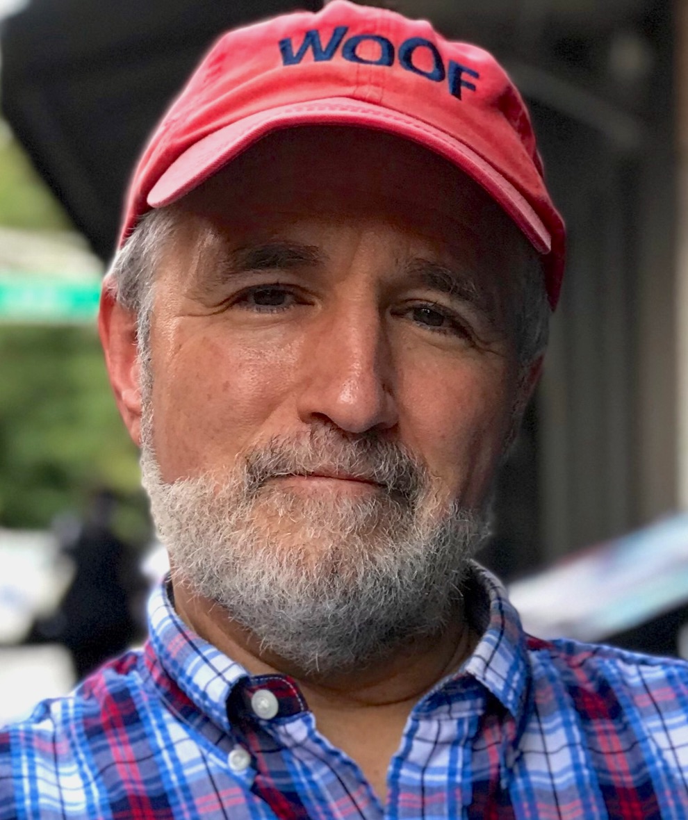 Headshot of Michael Snow wearing a red baseball had that says "Woof" in dark letters. 