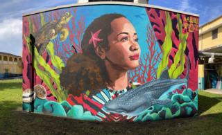 An outdoor mural of a woman surrounded by a whale and marine plants
