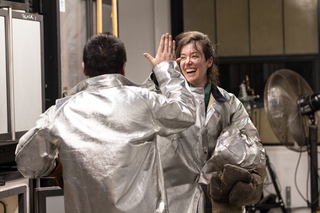 Two students in protective gear in the hot shop high five-ing  